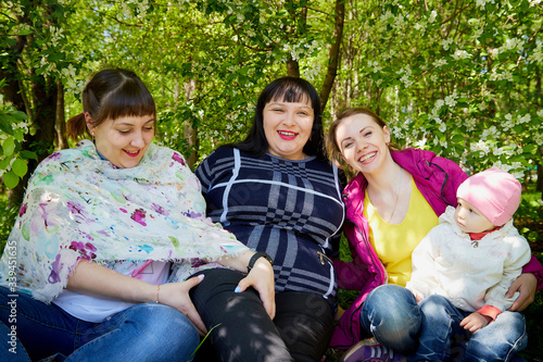 Three different funny women and one small seriously girl in the park full of apple blossom trees in a spring day. Aunts and niece in nature landscape © keleny