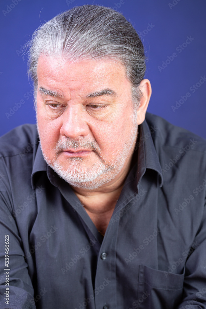 Man studio closeup portrait. He is pensive and looking down. The background is lighted with blue color.