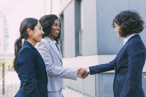 Interracial business partners greeting each other near office building. Business women wearing office suits, shaking hands with each other outside in city. Cooperation concept