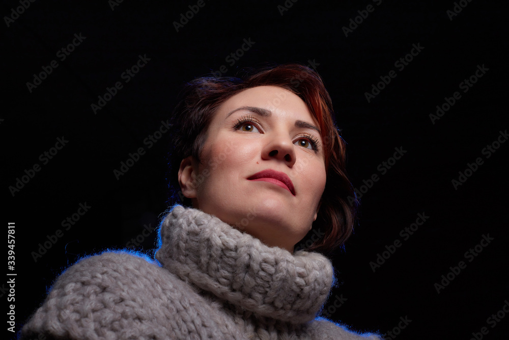 Portrait of a beautiful, charming young woman in in a grey thick knitted sweater and a black background. Model posing doring studio photo shot Portrait of a beautiful, charming young woman in in a grey thick knitted sweater and a black background. Model posing doring studio photo shot