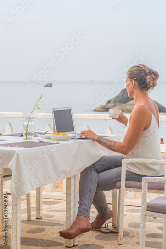 A woman sitting at a beach restaurant having breakfast while working on a laptop.