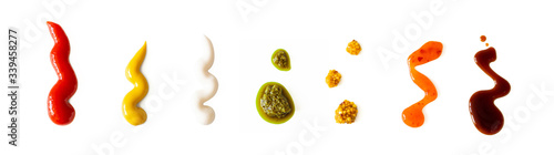 Ketchup, mustard, mayonnaise, basil pesto, sweet chili sauce and teriyaki soy sauce splash isolated on white background, top view. Various seasoning and dip border horizontal banner format