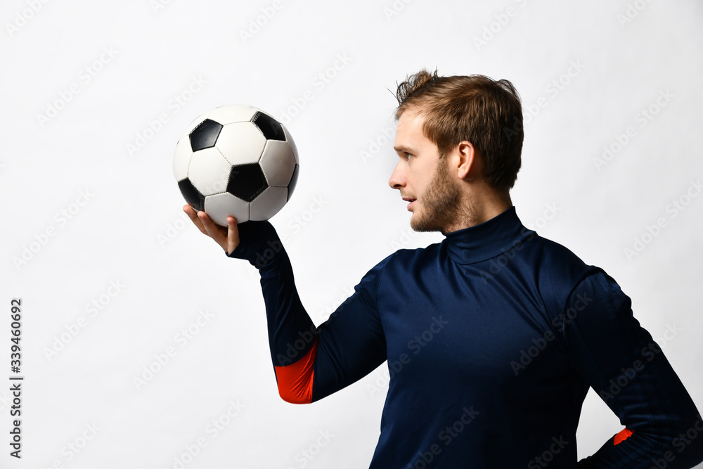 Blond man, professional soccer player in blue tracksuit is going to throw a ball, posing sideways isolated on white. Close up