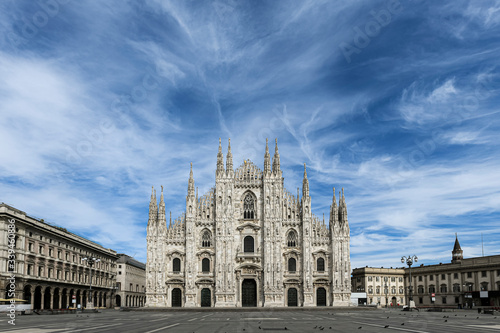 The gothic Duomo Cathedral facade in Milan, Italy on a beautiful spring day. Empty Duomo square. Blue sky with scattered soft clouds. 