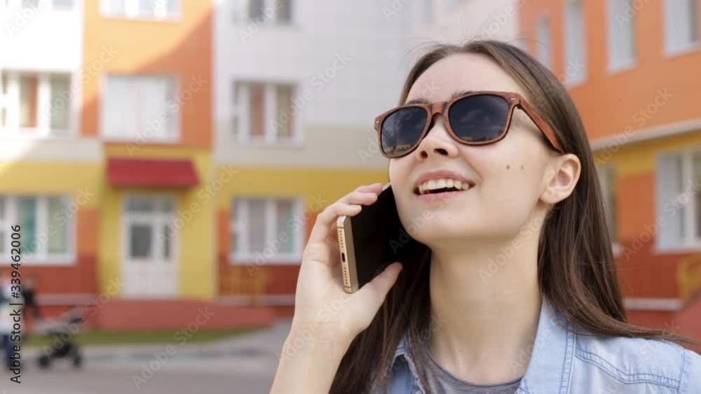 Smiling young woman in eyeglasses talking on phone near office building. Joyful female freelancer in casual wear speaking on smartphone and looking at sky while standing near business center Smiling young woman in eyeglasses talking on phone near office building. Joyful female freelancer in casual wear speaking on smartphone and looking at sky while standing near business center