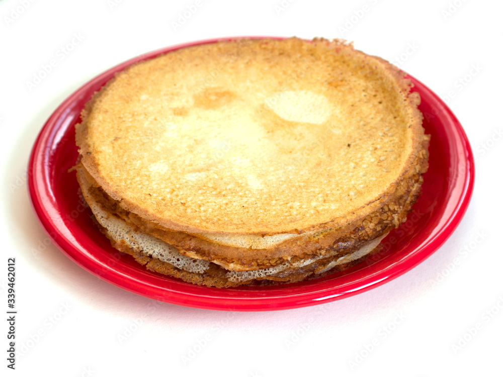 Staple of wheat golden yeast pancakes or crepes on red plate on a white background closeup Staple of wheat golden yeast pancakes or crepes on red plate on a white background closeup