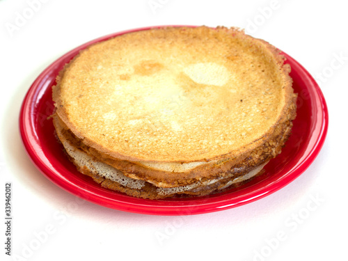 Staple of wheat golden yeast pancakes or crepes on red plate on a white background closeup