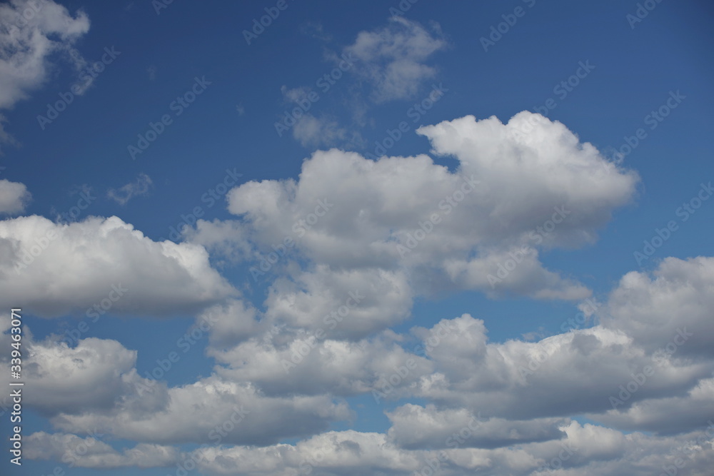 Obraz premium The sun shines through the cumulus clouds in the blue sky. Background and texture for artists and design. Bright light in the eyes. Water in gaseous state. The circulation of fluid in nature