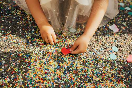 Close up of multi-colored rice cover the ground after a wedding ceremony. Hands of girl hold red heart.