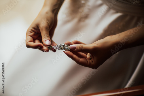 Elegant bride holding silver earrings. Hands with jewelry.  Wedding morning preparation in home. Bridal getting ready.  Earrings close-up in the hands of the bride. Jewelry accessories.