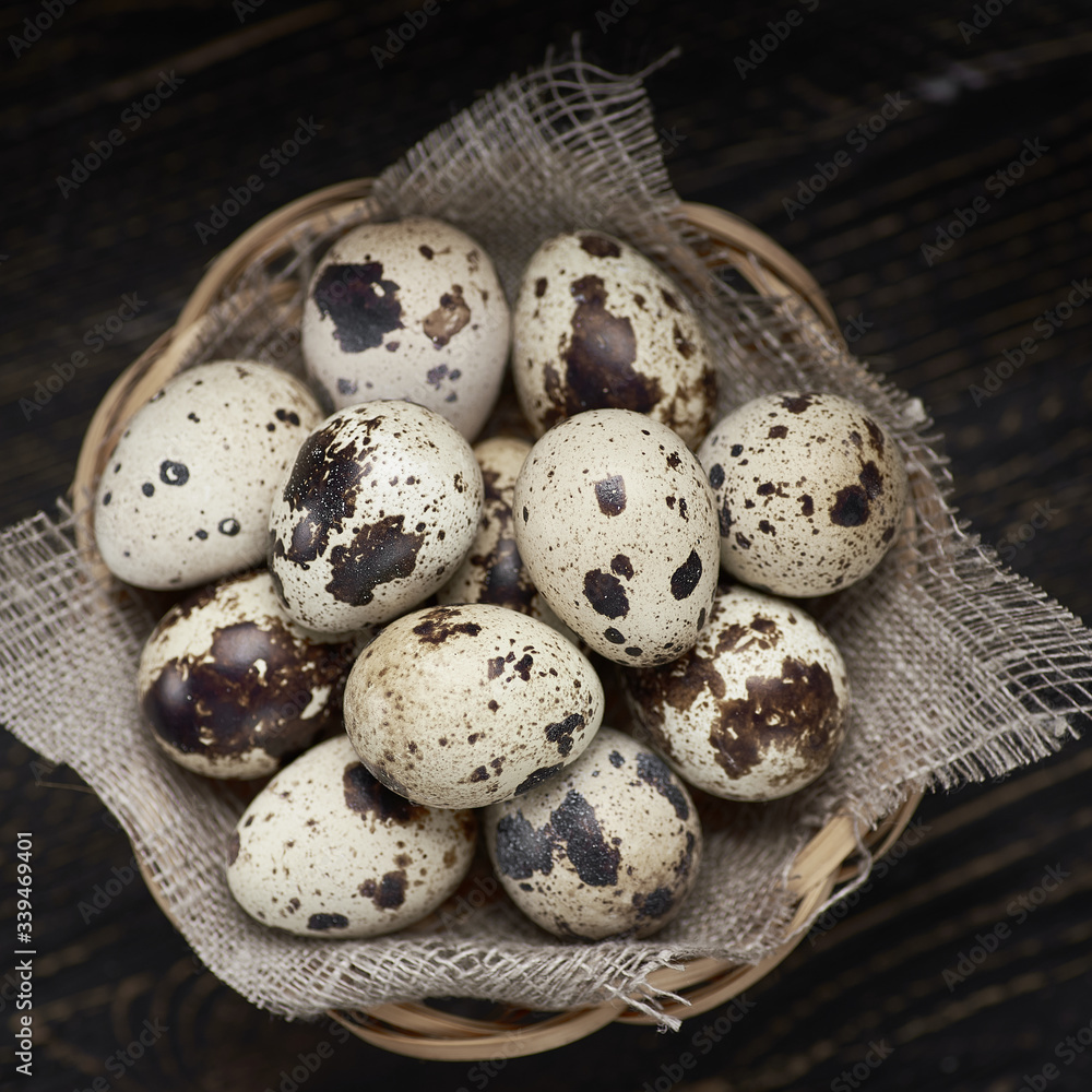 Obraz premium Wicker basket canvas napkin filled with eggs of quails on wooden table.