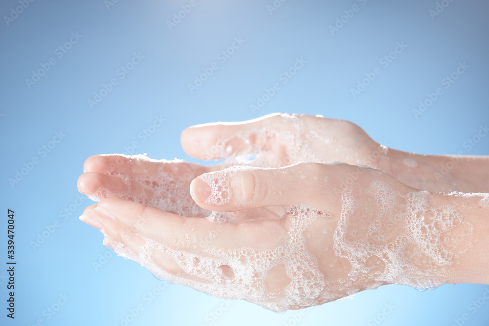 Woman's hands in soapsuds, on blue background close-up.