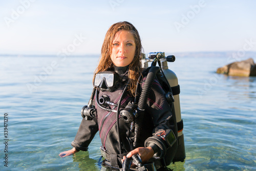 Female Scuba Diving Instructor Standing in Water Wearing a Dry Suit, a Twin Tank and Holding Fins © Angelina Cecchetto