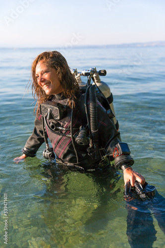 Female Scuba Diving Instructor Standing in Water Wearing a Dry Suit, a Twin Tank and Holding Fins