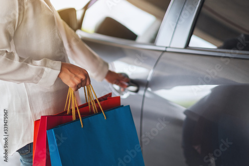 Closeup image of a woman holding shopping bags while opening car door in the mall parking lot