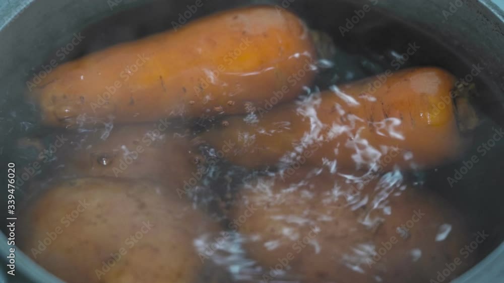 Peeled carrots and potatoes are boiled in a pan with water close up Peeled carrots and potatoes are boiled in a pan with water close up