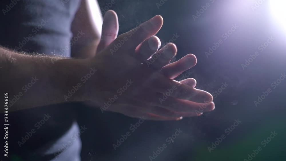 Close-up of sporty unrecognizable man clapping hands with talc and preparing for workout at gym. Closeup of athletic fitness male hands preparing for fit workout in gym with chalk magnesium carbonate.