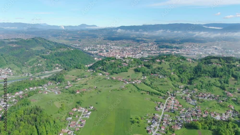 Hilly lush green landscape with small towns in the valley connected by winding roads on a sunny day. Aerial drone shot. Kočevje - Slovenia Hilly lush green landscape with small towns in the valley connected by winding roads on a sunny day. Aerial drone shot. Kočevje - Slovenia