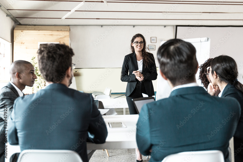 Smiling female business trainer working with employees. Group of workers sitting at table and listening speaker. Business meeting concept Smiling female business trainer working with employees. Group of workers sitting at table and listening speaker. Business meeting concept