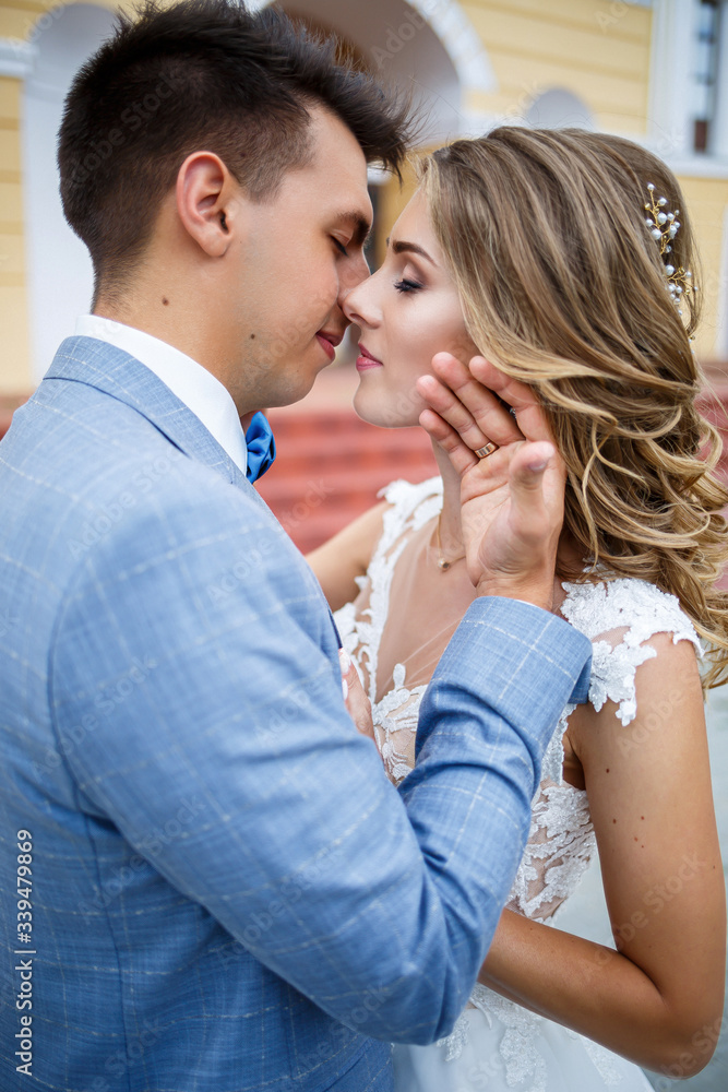 Young stylish guy in the costume of the groom and the bride beautiful girl in a white dress with a train walking on the background of a large house with columns on their wedding day Young stylish guy in the costume of the groom and the bride beautiful girl in a white dress with a train walking on the background of a large house with columns on their wedding day