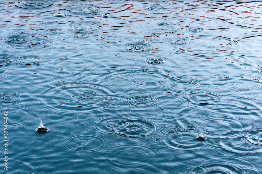 rain drops on the surface of water in a puddle with graduated shade of black shadow and reflection of blue sky rain drops on the surface of water in a puddle with graduated shade of black shadow and reflection of blue sky
