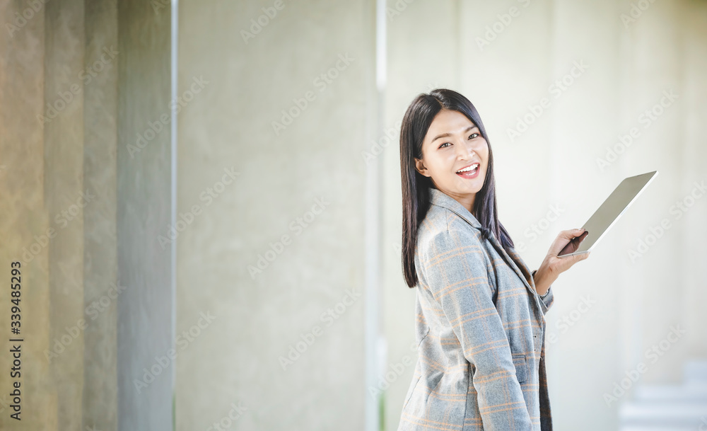 Portrait of business woman looking digital tablet with white travel bag on walkway while waiting to travel to the destination Portrait of business woman looking digital tablet with white travel bag on walkway while waiting to travel to the destination