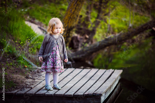 little cute girl standing on wooden bridge on pond