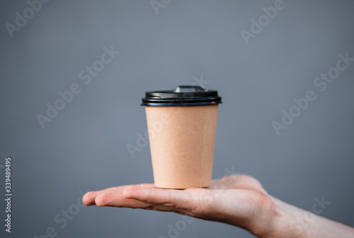 Cup of coffee on the palm of a man. Cup of coffee. Coffee. Cardboard cup. Gray background.