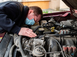 Mechanic in protective medical mask checks car engine