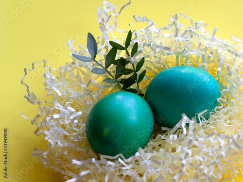 Colorful easter eggs in paper nest decorated with flower and leaves on yellow pastel background. Haapy easter! easter greeting card photo