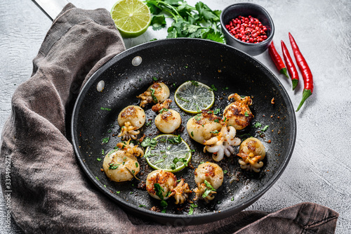 Mini grilled squid with lime and spices in a pan. Gray background. Top view
