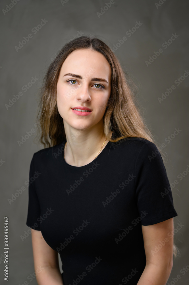 Vertical portrait of a caucasian girl in a black dress with long hair on a gray background. Vertical portrait of a caucasian girl in a black dress with long hair on a gray background.