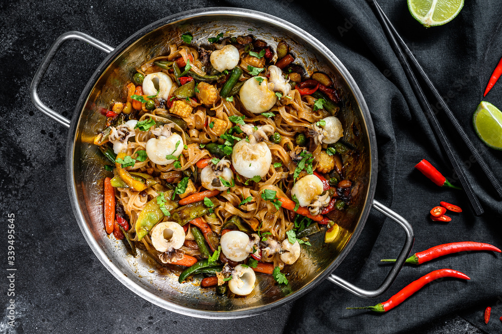 Stir fry noodles with seafood and vegetables in a wok pan. Black background. Top view