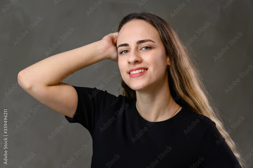 Portrait Caucasian happiness girl in a black dress with long hair and a beautiful smile with straight teeth on a gray background. Portrait Caucasian happiness girl in a black dress with long hair and a beautiful smile with straight teeth on a gray background.