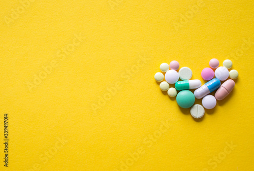 Pharmaceutical medicine pills in a small heart-shaped over yellow backgroud