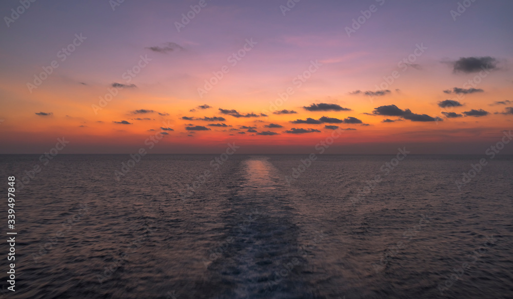 Remarkable vibrant colorful sunset or sunrise and ship cruising trail enjoyed from boat ride in open seas in Indonesia