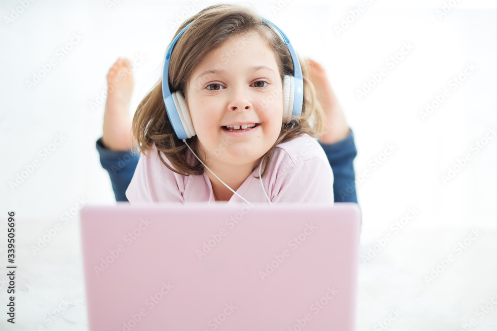 Smiling happy schoolgirl in headphones on a pink computer laptop, studying online , enjoys music, uses the video call application, listens to music, reads, e-books.Concept of online learning Smiling happy schoolgirl in headphones on a pink computer laptop, studying online , enjoys music, uses the video call application, listens to music, reads, e-books.Concept of online learning