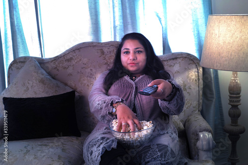 Young fat woman watching TV and eating popcorn photo