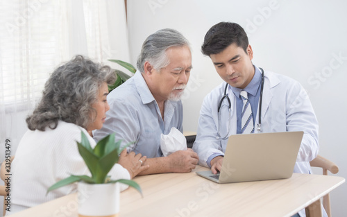 Caucasian doctor use laptop and talk with old asian male patient about disease symptom, elderly health check up at home.
