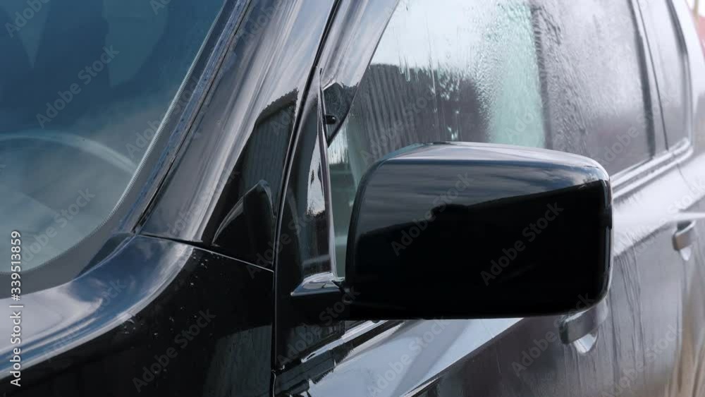 Closeup of modern vehicle washed by anonymous person with high pressure water. A very dirty car is cleaned with a jet of clean water Closeup of modern vehicle washed by anonymous person with high pressure water. A very dirty car is cleaned with a jet of clean water