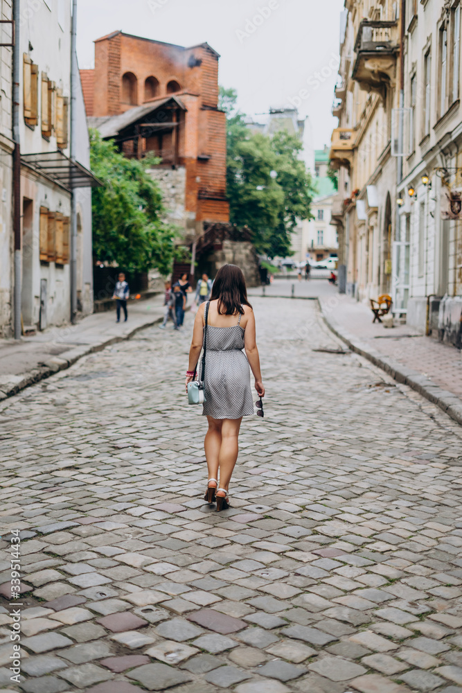 Young woman walking in the sunny city streets. Brunette woman in sundress and sandals.
