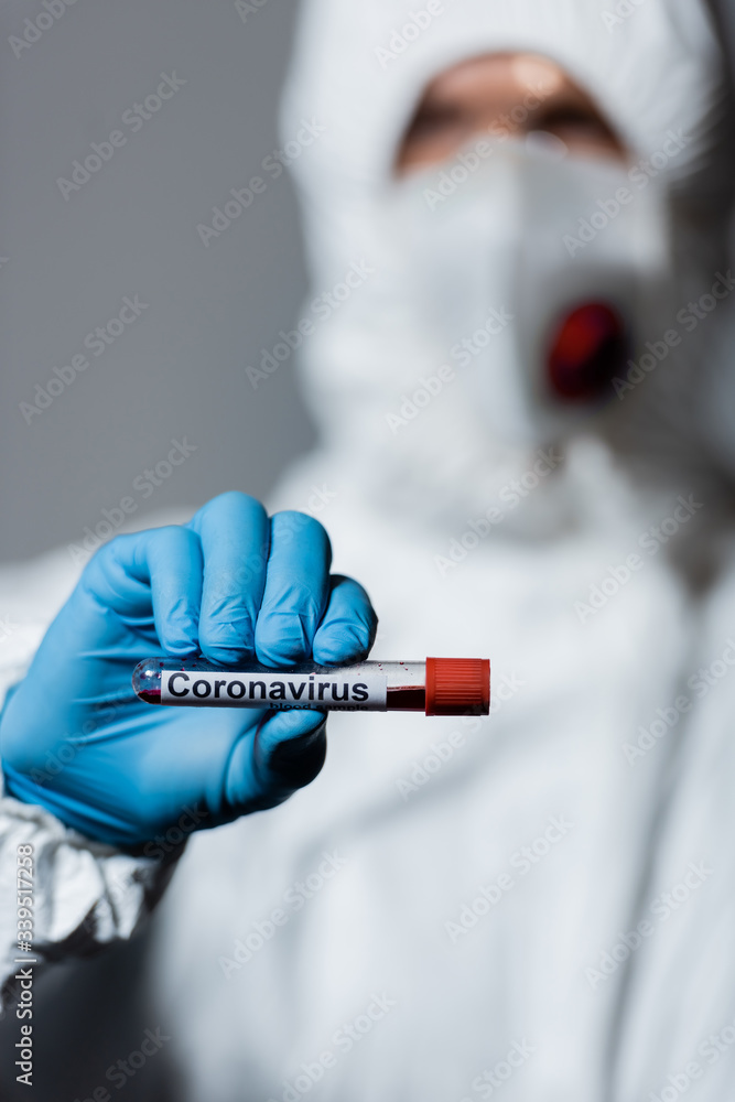 selective focus of mature doctor in hazmat suit, medical mask and goggles holding test tube with coronavirus lettering isolated on grey selective focus of mature doctor in hazmat suit, medical mask and goggles holding test tube with coronavirus lettering isolated on grey