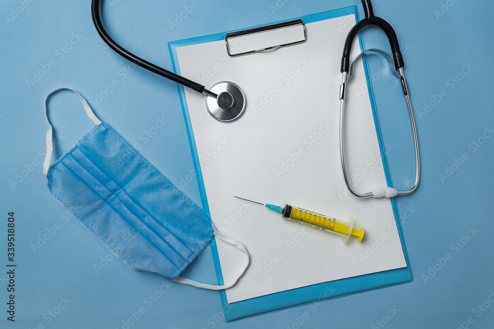 Stethoscope, medical mask, syringe and empty sheets of paper on blue background. Copy space. Mock up. Flat lay Stethoscope, medical mask, syringe and empty sheets of paper on blue background. Copy space. Mock up. Flat lay