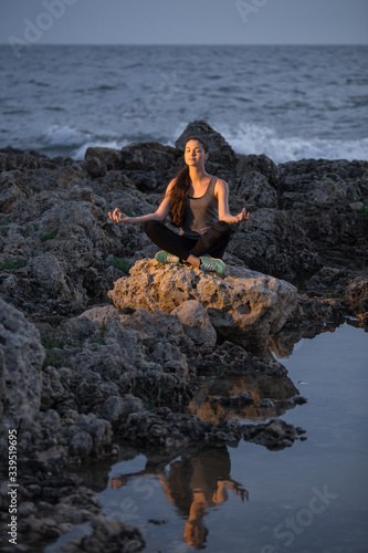 Yogi girl in lotus pose on the rocks near the sea at night photo