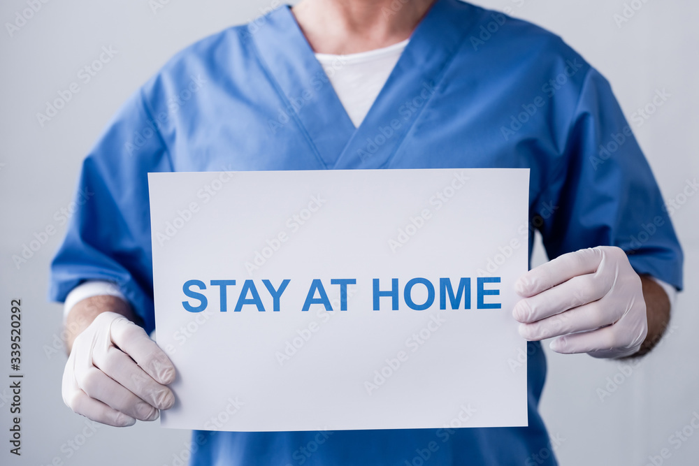 cropped view of mature doctor holding placard with stay at home lettering on grey cropped view of mature doctor holding placard with stay at home lettering on grey