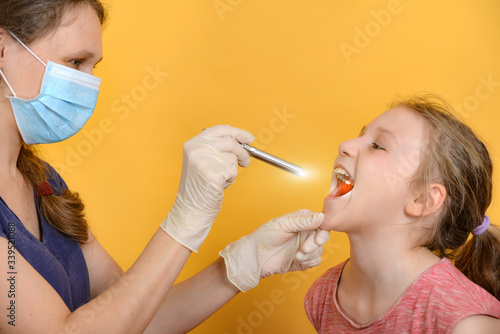 Fotografie A female doctor examines a girl's oral cavity with a diagnostic medical flashlight