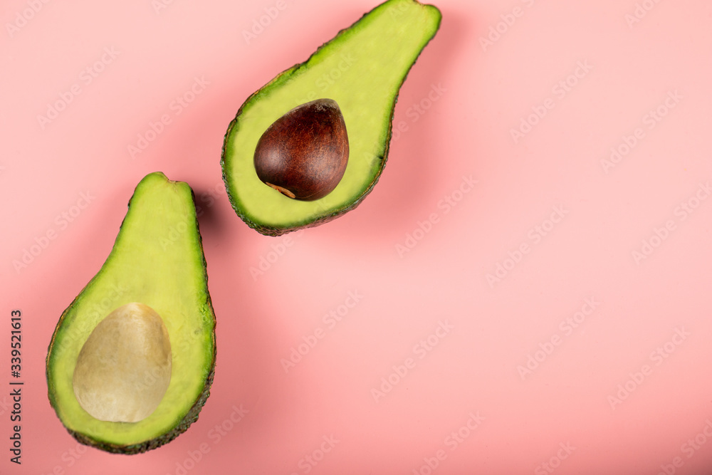 Green half avocadoes with and without seed, top view on pink