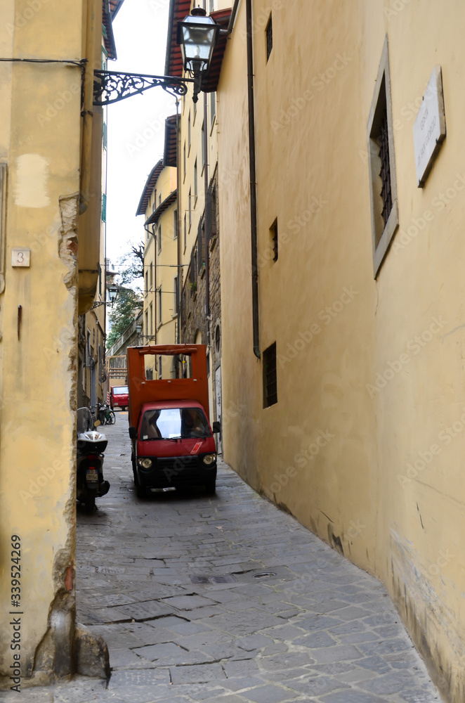 Sunny alley in Florence wiht 
red car, Italy