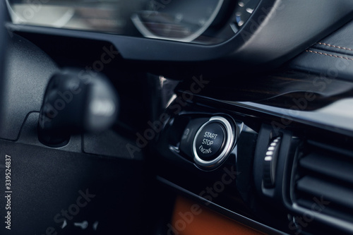 Car Start-Stop Engine Button of a modern car in the interior of the expensive car. Black and brown leather car interior. Illuminated dashboard. Luxurious car instrument cluster. Close up