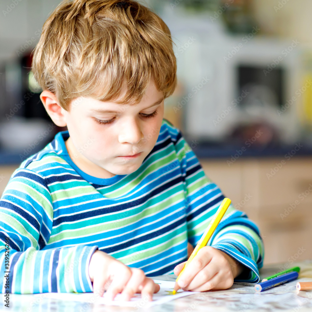 Hard-working happy school kid boy making homework during quarantine time from corona pandemic disease. Healthy child writing with pen, staying at home. Homeschooling concept Hard-working happy school kid boy making homework during quarantine time from corona pandemic disease. Healthy child writing with pen, staying at home. Homeschooling concept